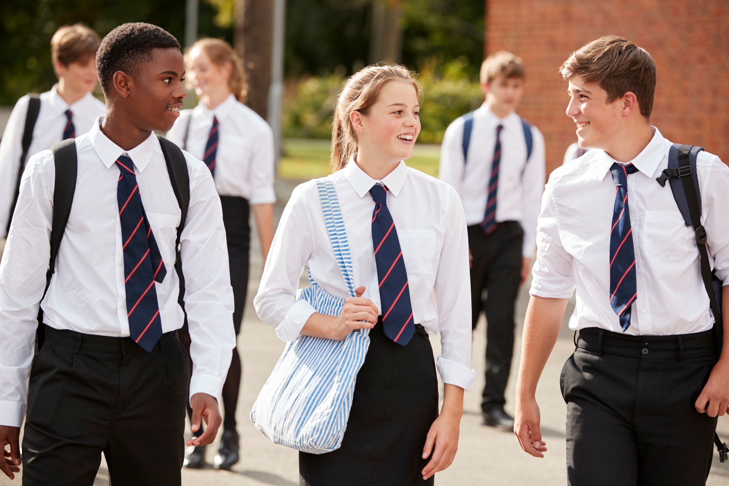 Three school students in school uniform, walking outside and talking