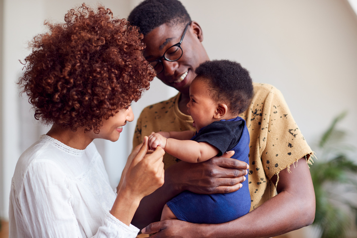 Two parents holding and playing with their young baby. 