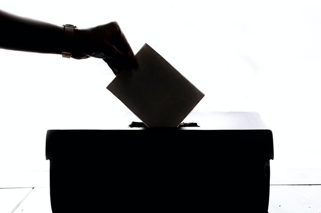 A silhouette of a hand dropping a paper into a ballot box