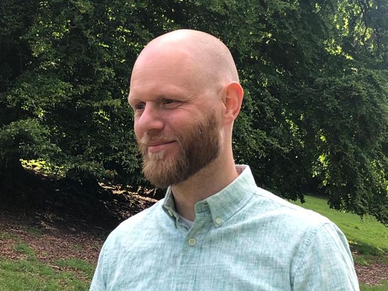 Bald man with dark beard, smiling and wearing a green shirt
