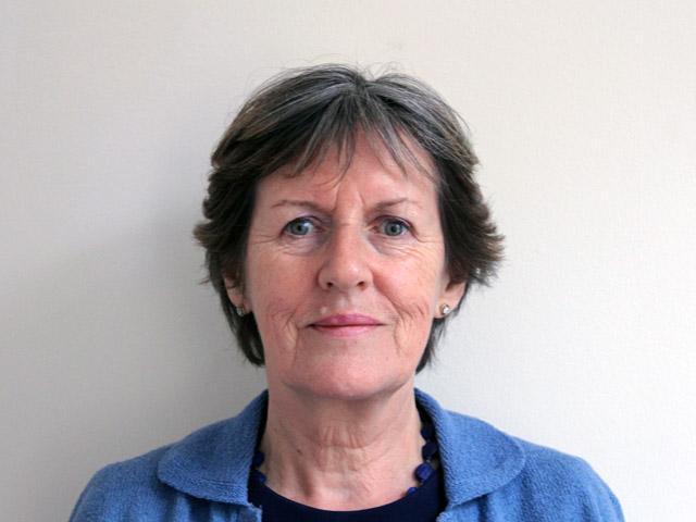 Woman with short dark grey hair looking directly at the camera and wearing a dark blue shirt
