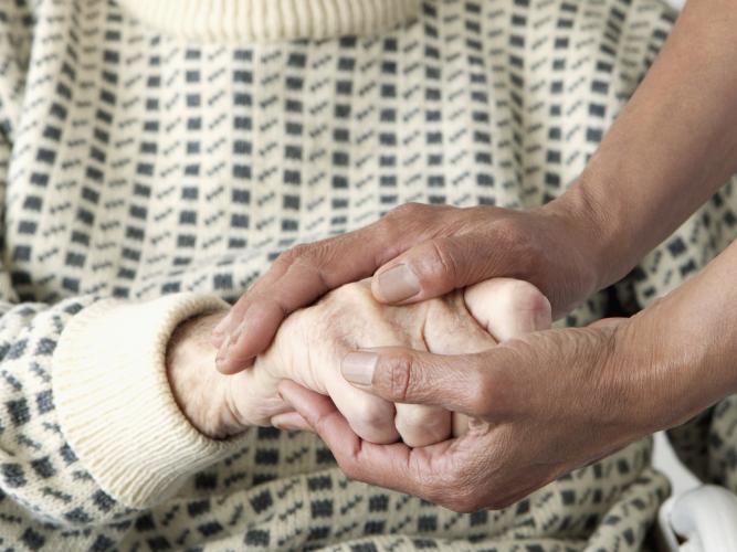 A close-up of a care worker patting an older man's hand.