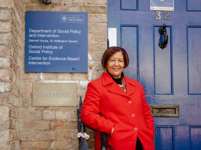 Laetitia Rispel wearing a red coat standing outside the blue door of Barnett House