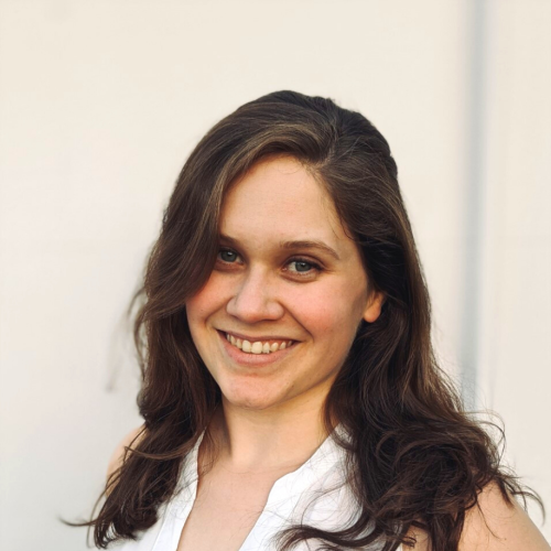 Anja is smiling widely at the camera. She has long dark hair and is wearing a sleeveless white blouse. 