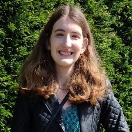 Chloe Brimicomb has shoulder-length brown hair and is wearing a blue jacket, standing in front of a green background