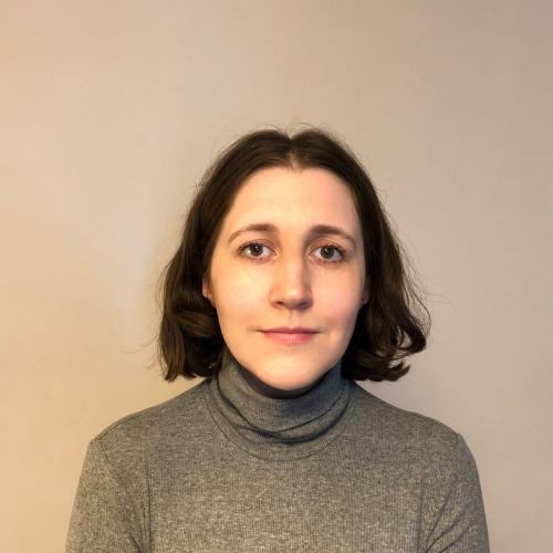 Lydia Holland has should length dark hair and is wearing a grey polo neck jumper. 