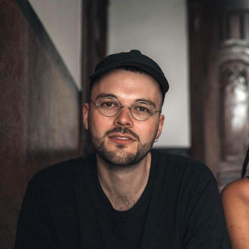 steffen has short black hair, black beard and metal-rimmed glasses. He's wearing a black jumper 