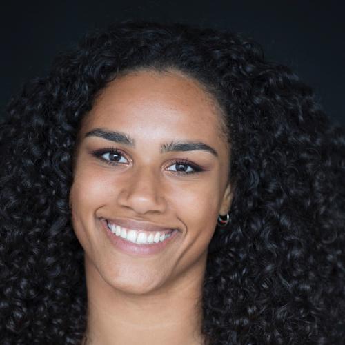 Hannah van Vijfeijken has shoulder-length dark curly hair and is smiling at the camera. She is wearing a red top. 