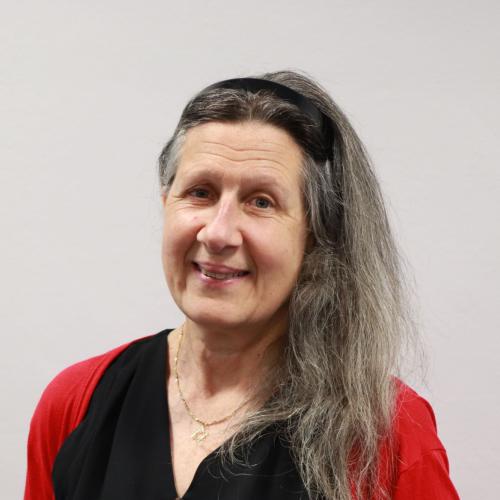 Louise Gordon has long grey hair and is smiling at the camera. She's wearing a black top with a red cardigan. 
