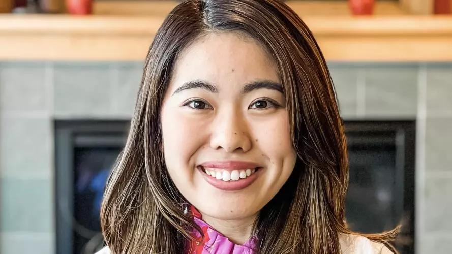 Hinako has long dark brown hair and is smiling at the camera. She's wearing a pink patterned blouse with a white cardigan. 