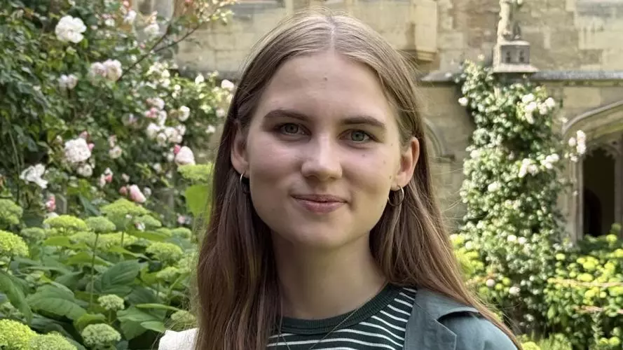Liina stands in college grounds. She is wearing a striped tee-shirt and has long, fair hair.