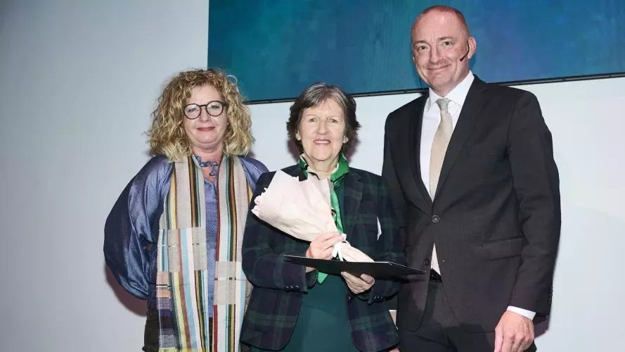 Three people are standing together at an award ceremony. Prof Daly is in the centre with short grey hair and wearing a dark checked jacket.