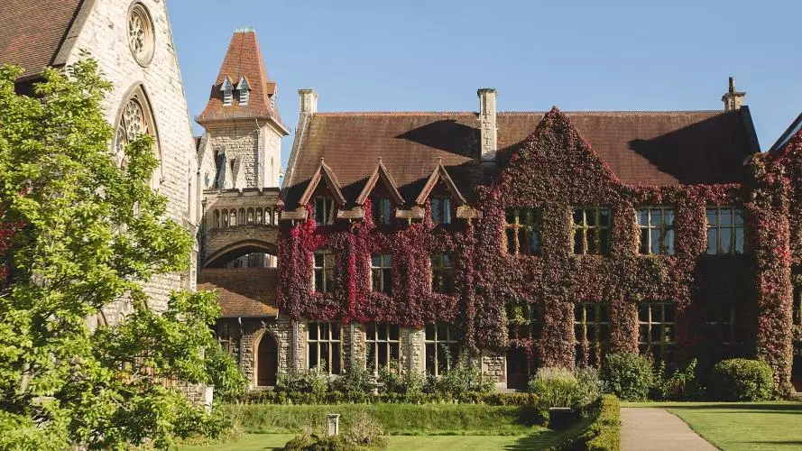 An ornate stone building in Cheltenham Ladies College, covered in ivy and with a lawn in front