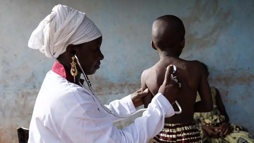 A nurse in a white uniform pressing a stethoscope to the back of a young child's back. Credit: Riccardo Niels Mayer - stock.adobe.com