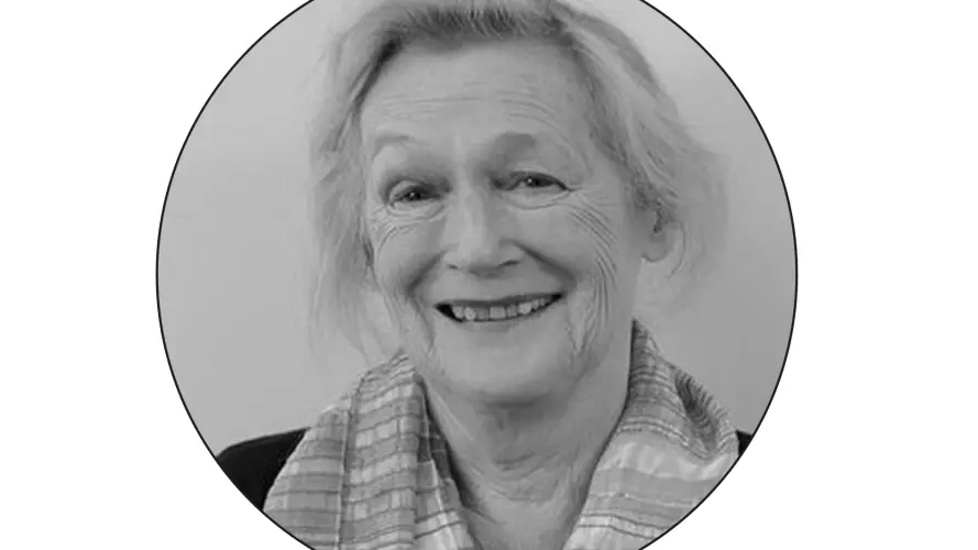 A black and white photo in a round photo frame of  Ann Buchanan wearing a suit smiling