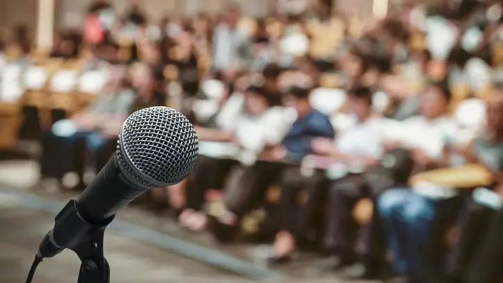 A close up of a microphone, in front of a large seated audience. Credit: Tzido - Getty Images-829570660
