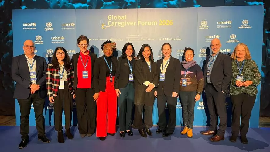 A group of ten, smartly dressed people stand in front of a sponsorship banner at the Global Caregiver Forum in Madrid
