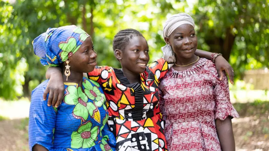 Three adolescent girls in colourful outfits. The girl in the middle has her arms around the shoulders of her friends either side. Credit: stock.adobe.com / Riccardo Niels Mayer