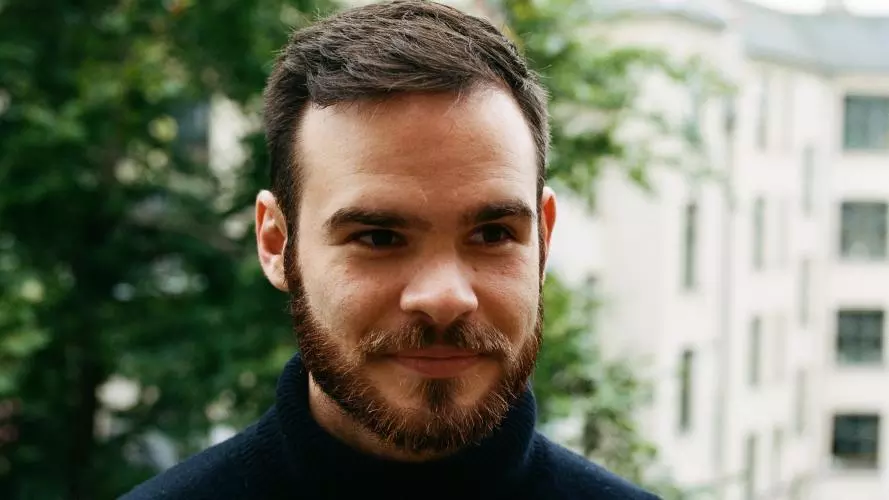 Man with dark brown hair and beard, wearing a black polo neck top