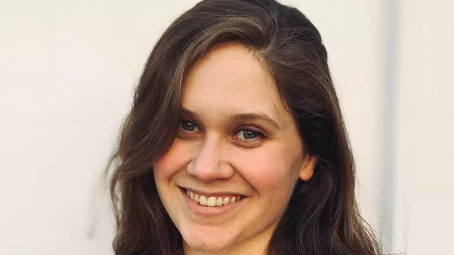 Anja is smiling widely at the camera. She has long dark hair and is wearing a sleeveless white blouse. 