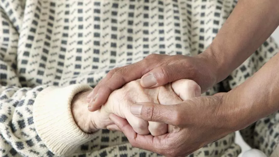 A close-up of a care worker patting an older man's hand.