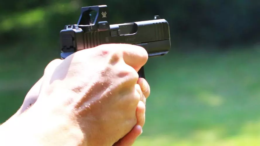 A man's hand holds out a handheld shotgun, aiming at nothing