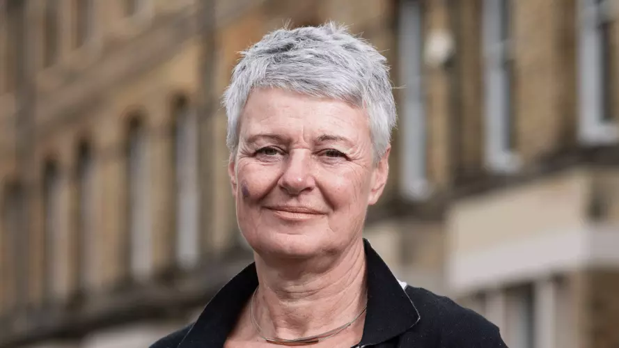 Jane Barlow is wearing a black top and jacket, with short gray hair, smiling for the camera.