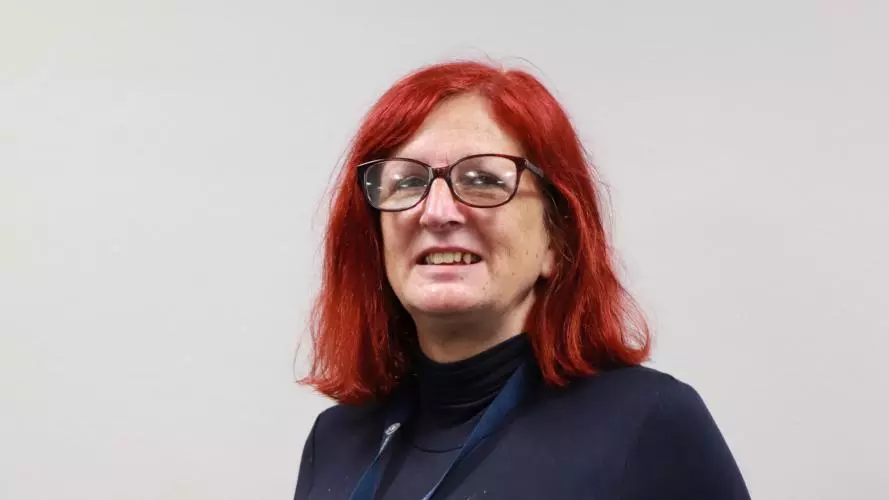 Woman with red hair and red rimmed glasses, who is smiling and wearing a dark top