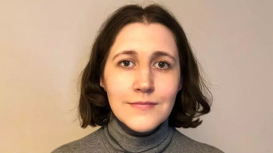 Lydia Holland has should length dark hair and is wearing a grey polo neck jumper. 