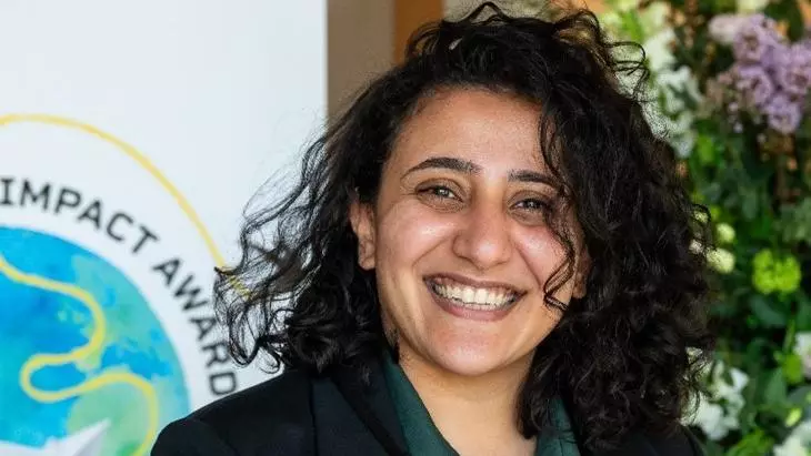 Dr Mona Ibrahim has shoulder-length curly black hair. She is smiling broadly, wearing a dark green blouse and black blazer.