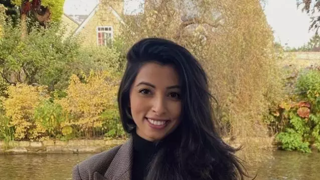 Saara has long dark hair, is wearing a brown suit jacket and is smiling at the camera. 