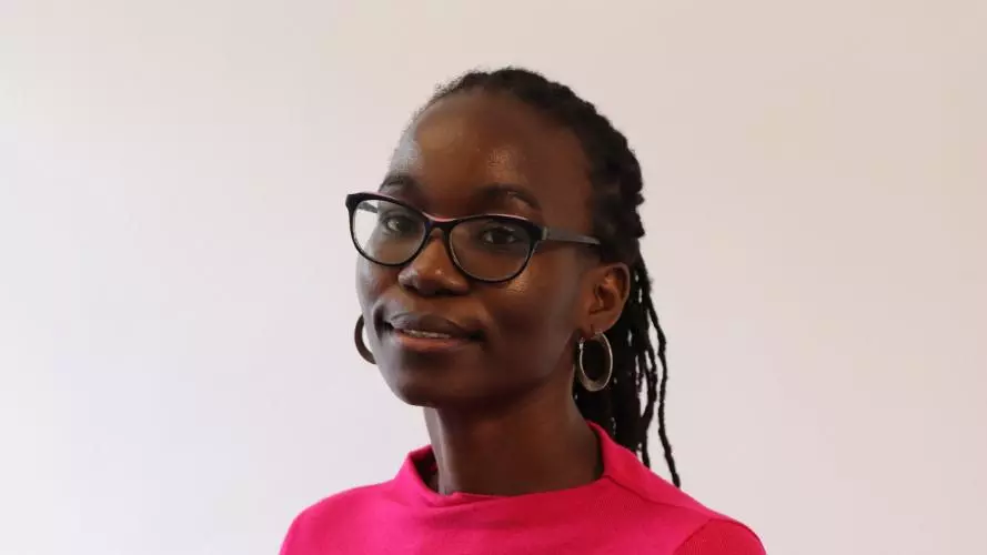 Yvonne has long black braided hair, is wearing glasses and a cerise pink top