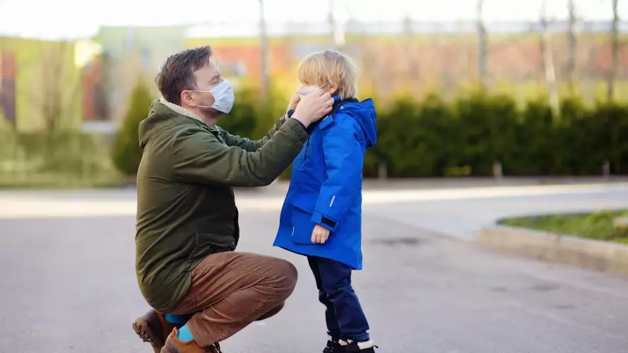 Father putting a protective face mask on his son.
