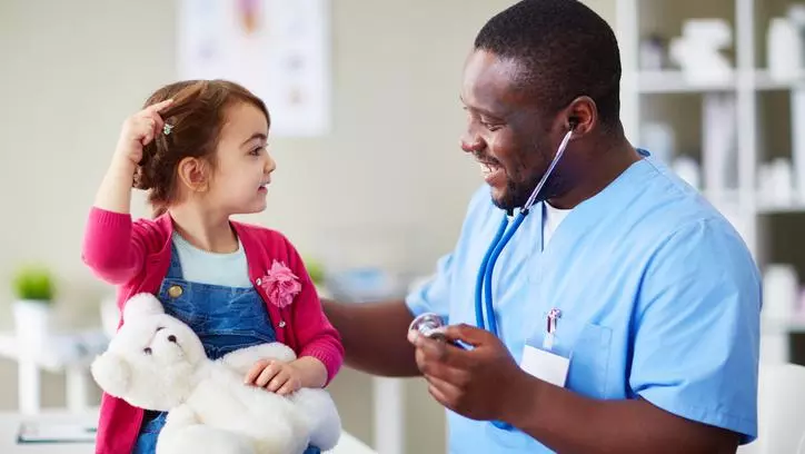 A young girl interacting with a healthcare worker, who is smiling and holding a stethoscope