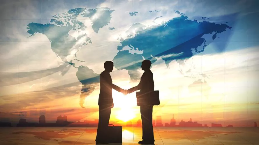 Global Business Elite Communities: Two people dressed in suits shaking hands against a world map