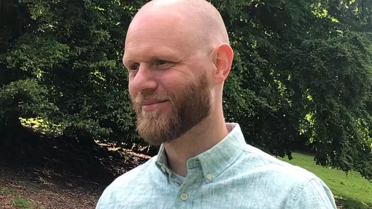 Bald man with dark beard, smiling and wearing a green shirt