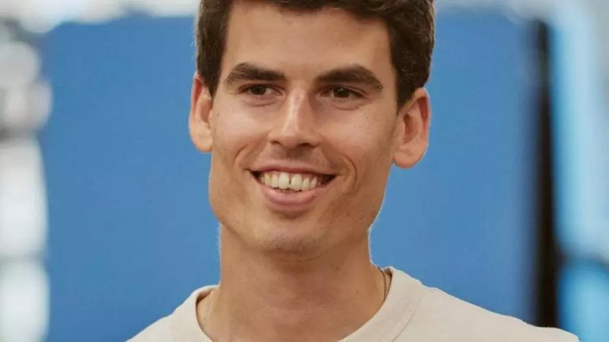 Alejandro has short brown hair, wearing a white t-shirt and smiling at the camera.