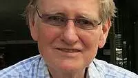 Patrick Casement has short grey hair. He is wearing thin, rectangular glasses and a blue checked shirt