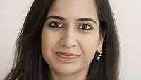 Maheen has long dark straight hair. She is wearing a white top. 