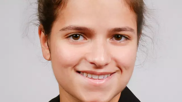 Woman who is smiling with brown hair tied back off her face and is wearing a black jacket