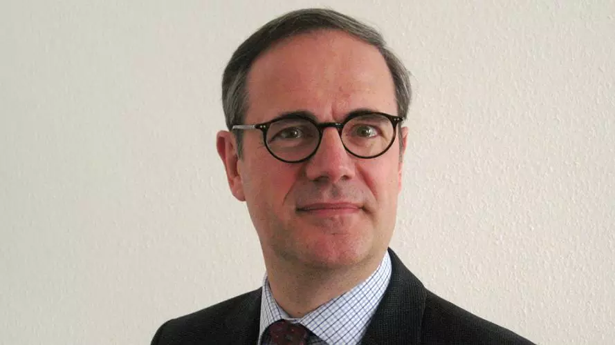 Man with dark grey wearing dark rimmed glasses and dark jacket