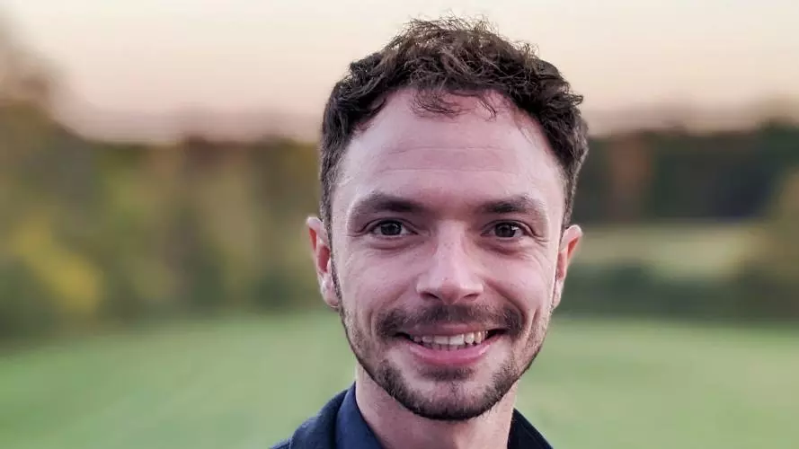 Hal Cooper, with short brown hair, is wearing a dark blue shirt and jacket, smiling at the camera