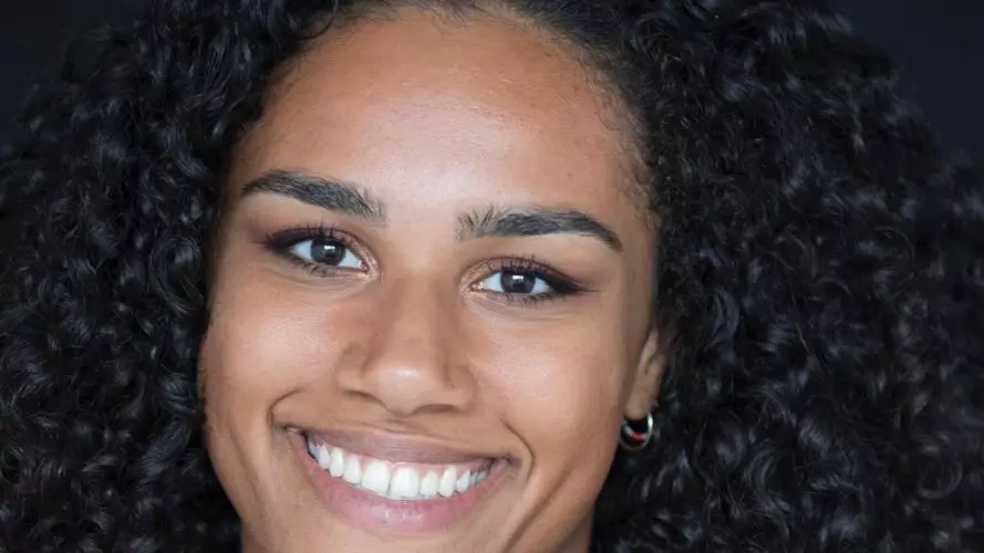 Hannah van Vijfeijken has shoulder-length dark curly hair and is smiling at the camera. She is wearing a red top. 
