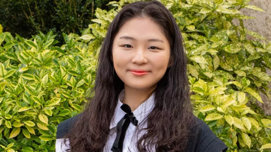 Jinseo Kim is wearing graduation gown, with dark shoulder length hair smiling at the camera.