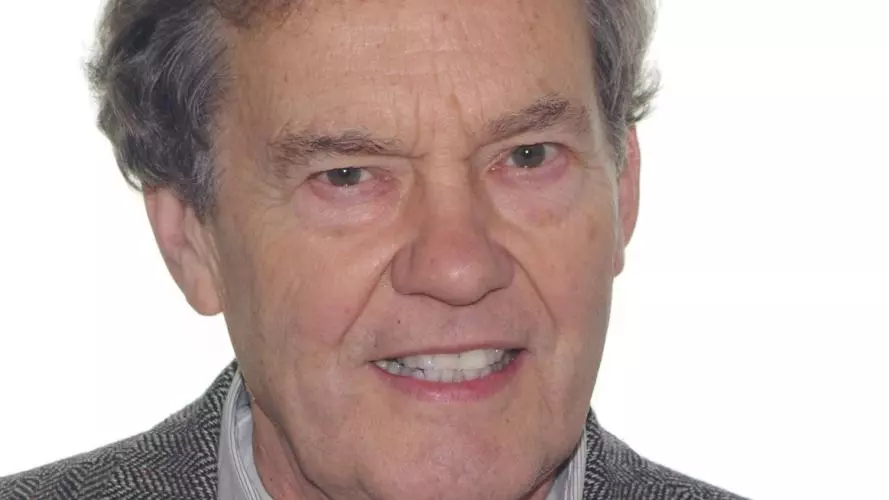 John Haskey has grey hair and is smiling at the camera. He is wearing a shirt and jacket.