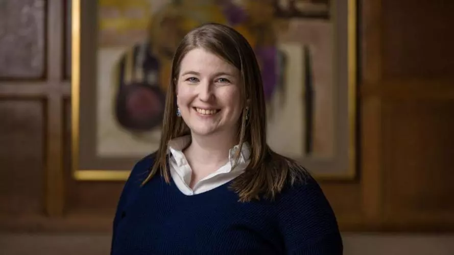 Julia has shoulder length ginger brown hair, with a dark top smiling at the camera.