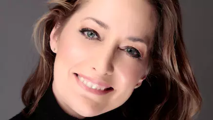 Karen has brown shoulder-length hair and smiling. She's wearing a black polo-neck top