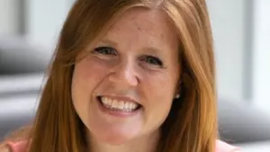 Kathleen is smiling  at the camera with long red hair smiling wearing a peach coloured top.