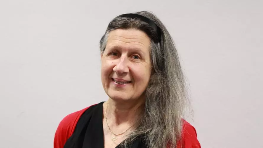 Louise Gordon has long grey hair and is smiling at the camera. She's wearing a black top with a red cardigan. 
