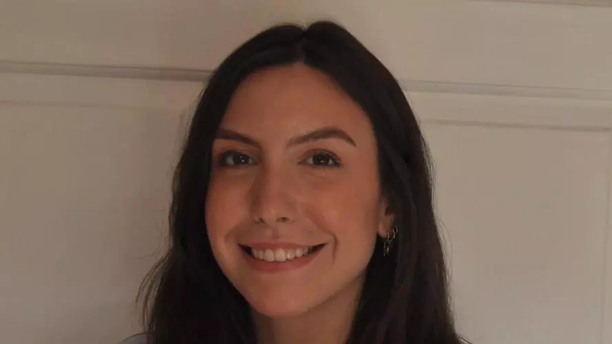 Luciana Leite has long dark hair and is wearing a light blue blouse. She is smiling at the camera.